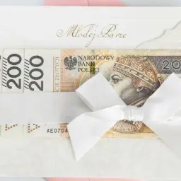 Biała koperta z napisem "Młodej Parze" i banknotami 200 zł, przewiązana białą wstążką. Pytanie, ile daje się na wesele, często sprowadza się do takiej właśnie formy prezentu.
