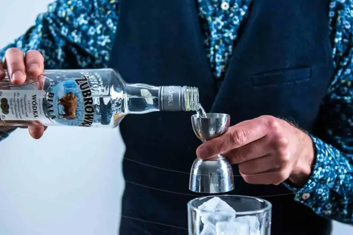 Wybierasz jaka wódka na wesele? Zubrówka Biała nalewana do jiggera, przygotowując drinka z lodem.