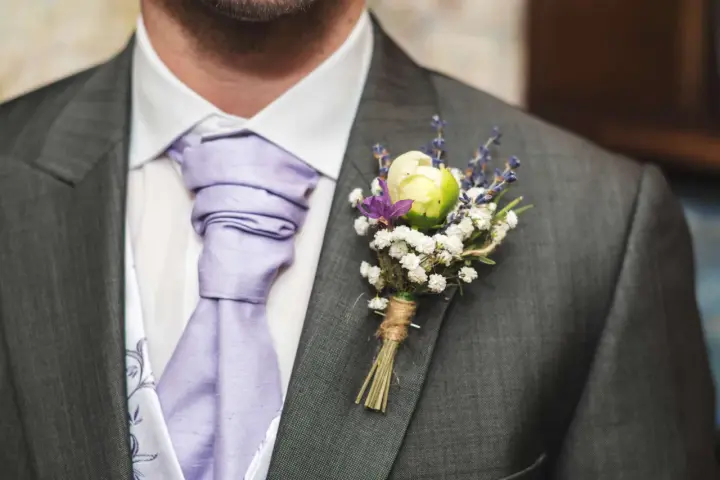 Elegancka butonierka co to? To ozdoba z kwiatów i lawendy przypięta do marynarki.