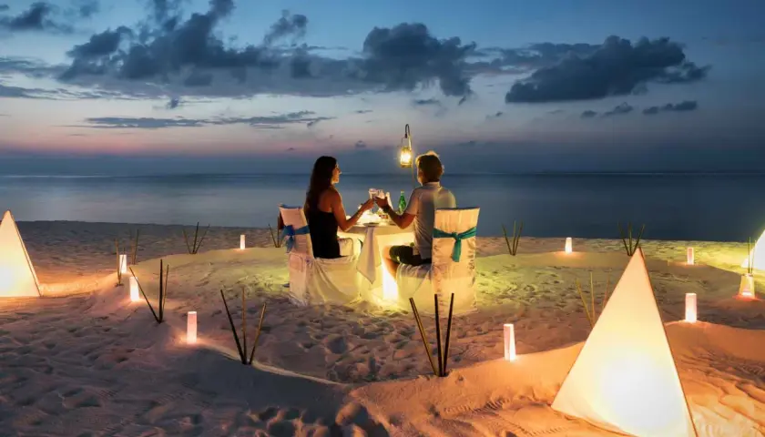 Romantyczna kolacja na plaży. Para świętuje 4 rocznicę ślubu przy blasku lampionów i zachodzącego słońca.