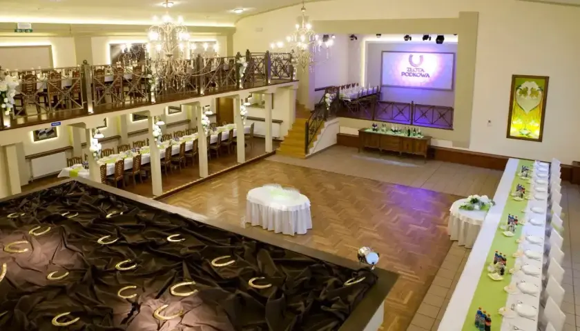 Elegancka sala weselna z podkowami szczęścia i stołami nakrytymi na przyjęcie.